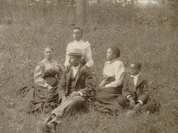 African American Family from late 1800's sitting on grass. 3 women, one man, and one young boy