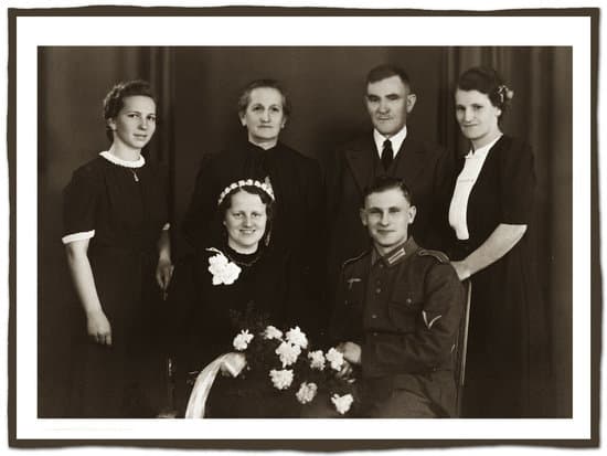 Black and white photo of bride and groom sitting and bride holding bouquet and parent behind them.