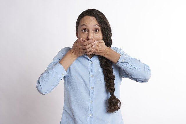 Woman in Blue shirt with hand over her mouth in a surprise expression