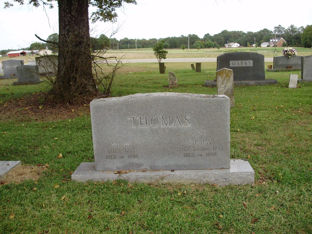 Gray gravestone with names of Sarah and Grisham Thomas in middle of cemetery with green grass.
