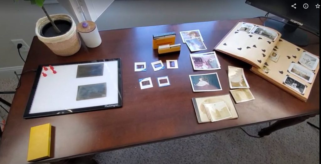 Desk with old family photos scattered on it. Includes light pad and old album