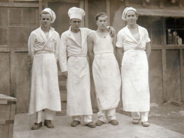 Black and white photo of four young men dressed as cooks including cook's hat