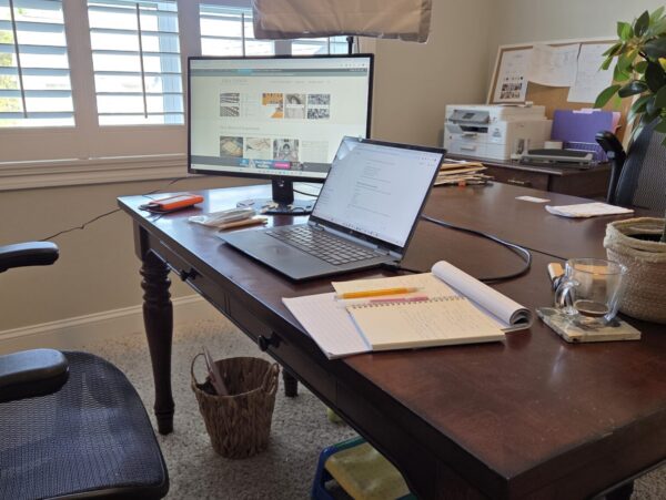 Office desk with laptop, second computer monitor and pens and paper